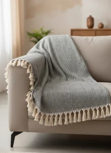 «نمای نزدیک شال مبل طرح زیگزاگ مشکی و سفید با ریشه‌های کرم روی مبل در نور طبیعی»