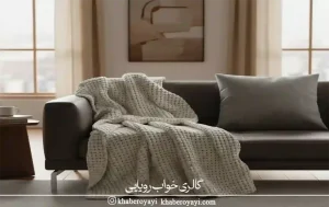 شال مبل بافت ضخیم کرم روی مبل طوسی که نمونه‌ای از بهترین جنس شال مبل برای فضاهای گرم و مینیمال است. 