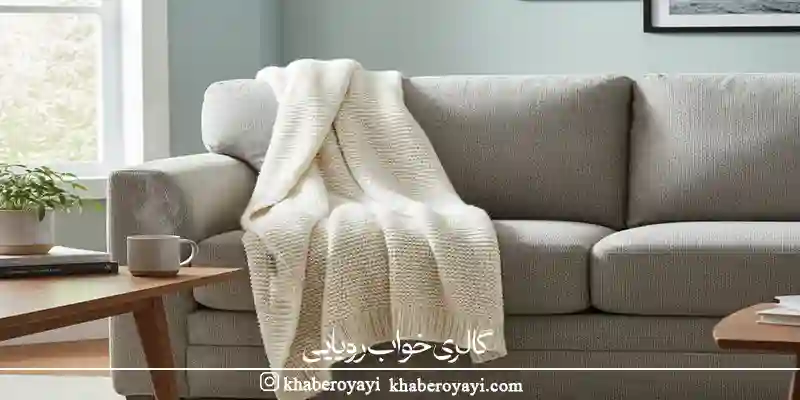 شال مبل روشن روی مبل طوسی در فضای گرم و خانگی، نمونه‌ای از نتیجه شستشوی شال مبل اصولی بدون افت کیفیت و تغییر رنگ